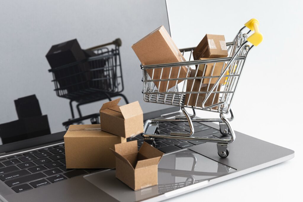 Um laptop com várias caixas e um carrinho de compras encima, simbolizando compras online. 
