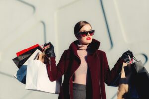 Mulher de batom e óculos escuros carregando sacolas de shopping